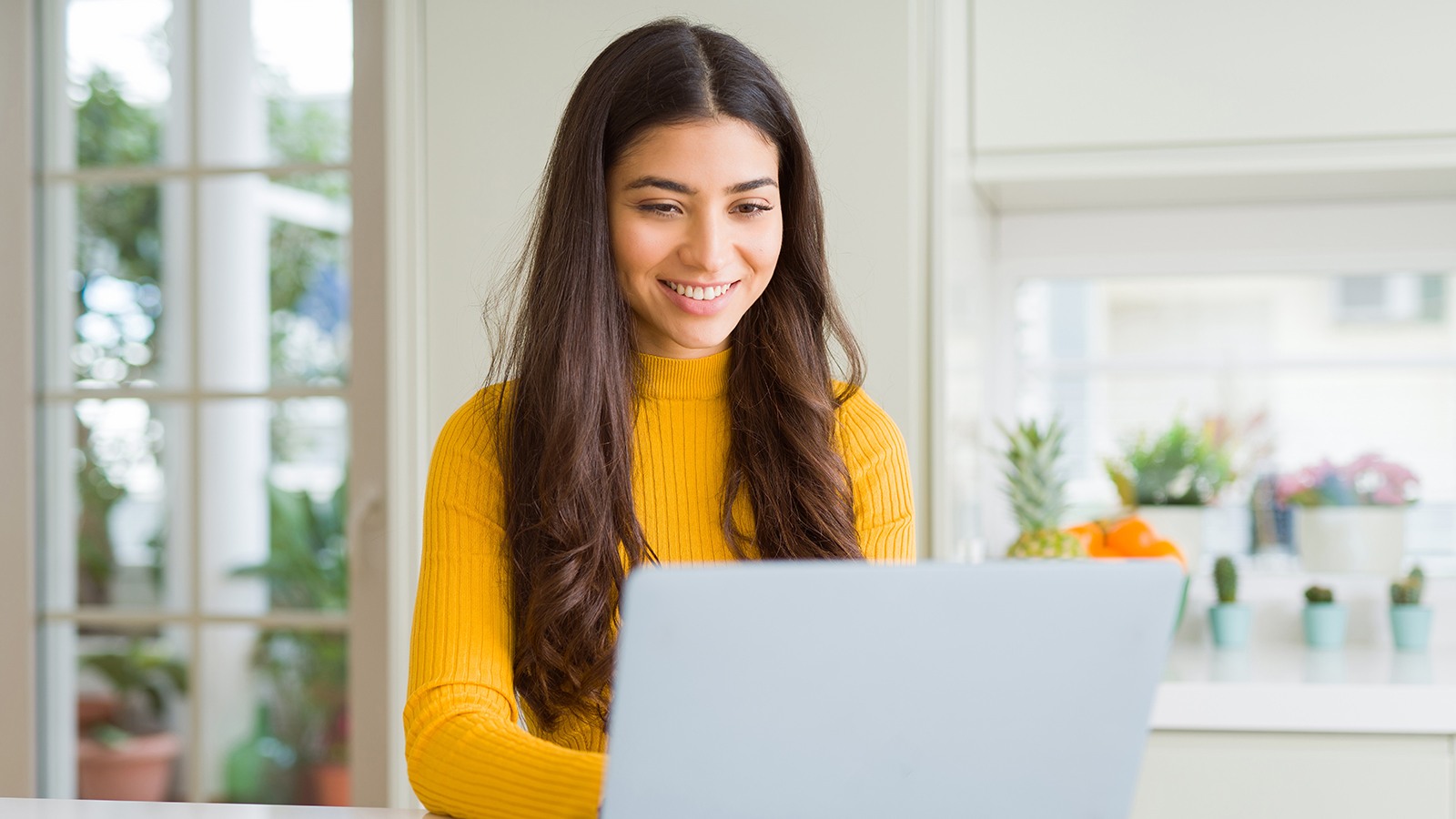 A woman in a light room sitting at the desk with her laptop