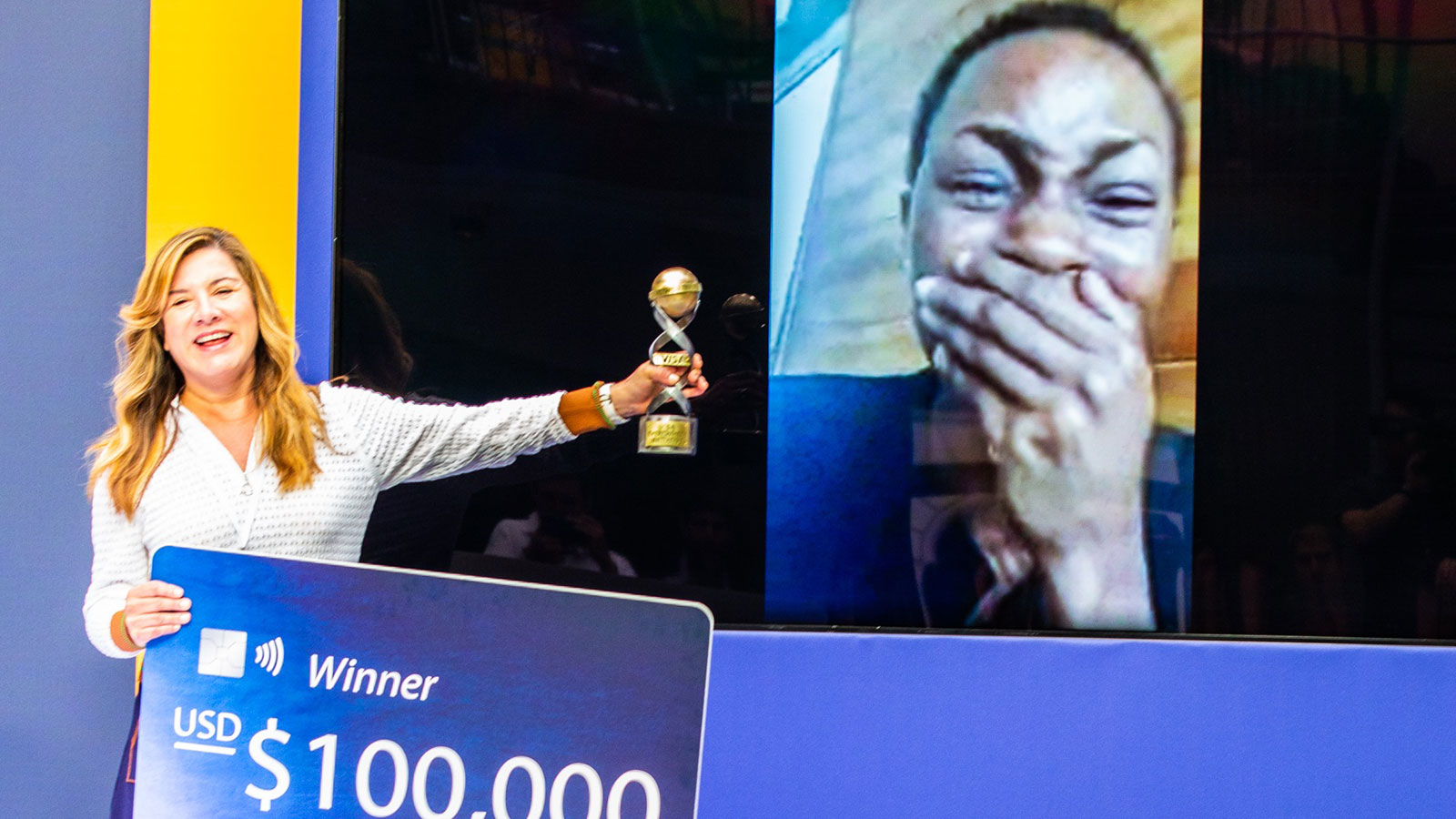 Woman presenting Monique Ntumngia, winner of the Social Impact challenge, a cutout of a Visa card worth $100k and a trophy.