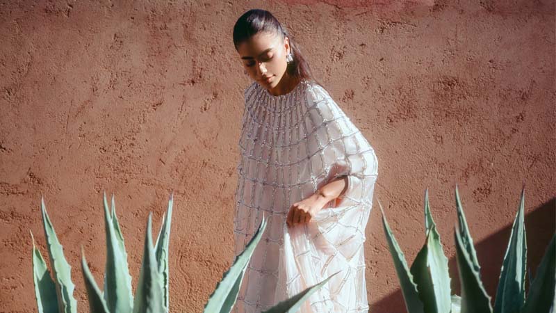 Woman in a white dress in the middle of the plants, with a wall in the background